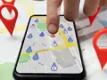 Dita la mappa con puntatori rossi, un dito tocca uno smartphone che mostra una mappa con gocce d'acqua, simulando gli spostamenti su Google Maps.