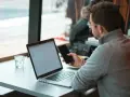 Uomo con occhiali che usa il telefono e il laptop, scopri come collegare il telefono al pc senza cavo per una maggiore comodità.