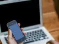 Persona che cerca su un laptop come attivare il microfono su Google, tenendo in mano uno smartphone.