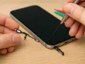 Riparazione tasto accensione rotto: un tecnico con pinzette e cacciavite lavora su un telefono, tenendo in mano il componente del tasto.