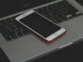 Un iPhone con cover rossa giace spento sulla tastiera di un MacBook.