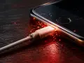 Un cavo di ricarica danneggiato provoca scintille e fiamme vicino alla porta del telefono, suggerendo una scheda madre del telefono bruciata.