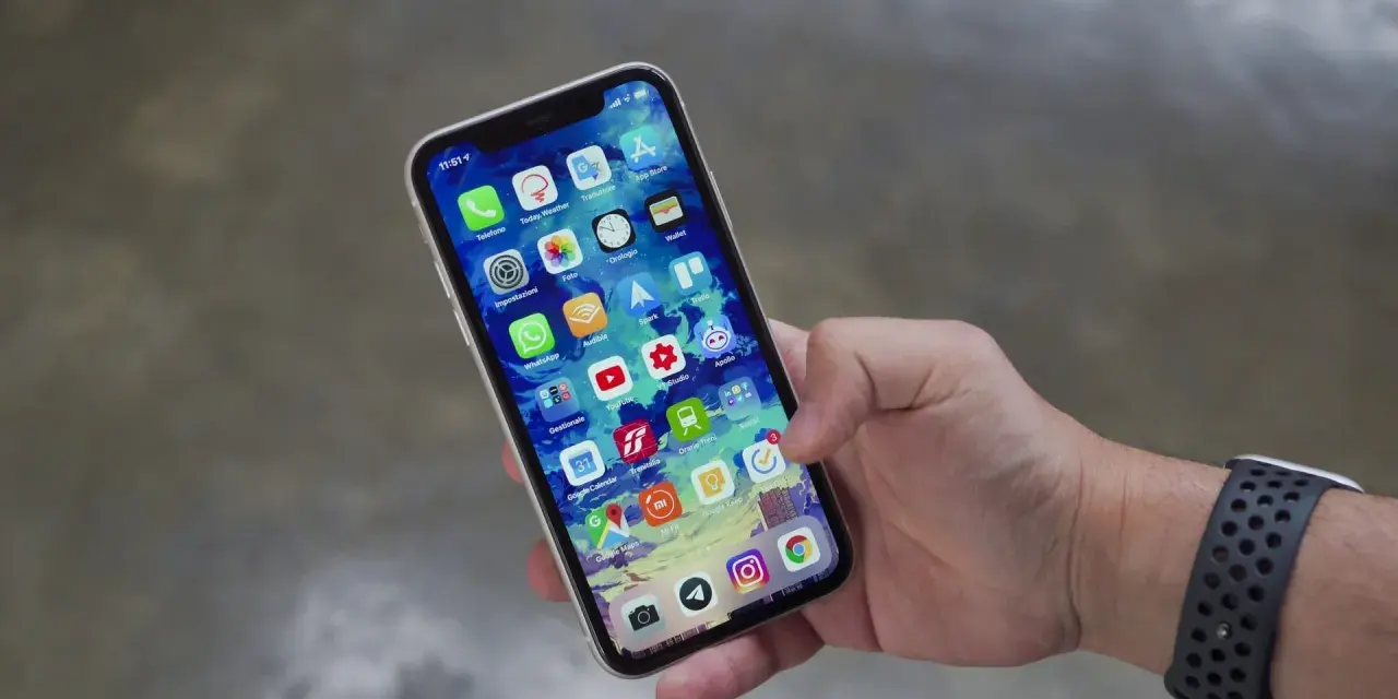 Mano che tiene uno smartphone con icone app. Potrebbe indicare problemi dopo sostituzione display, con alcune icone che appaiono leggermente sfocate o distorte.