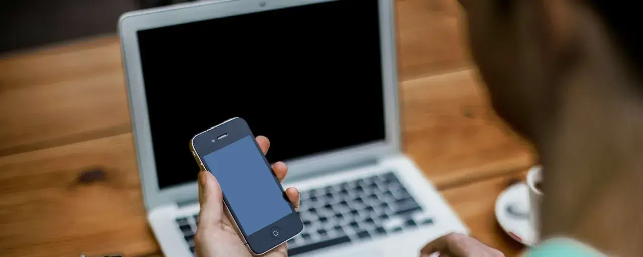 Persona che cerca su un laptop come attivare il microfono su Google, tenendo in mano uno smartphone.