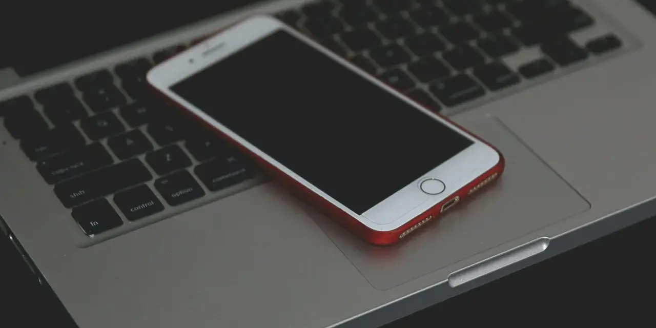 Un iPhone con cover rossa giace spento sulla tastiera di un MacBook.