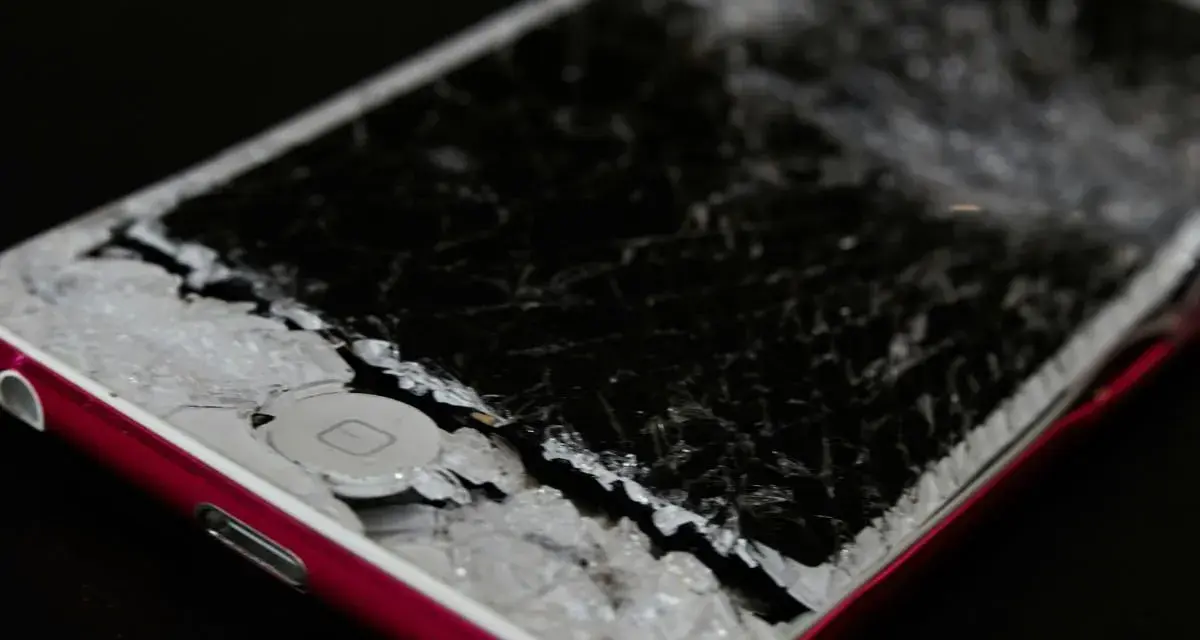 Cellulare caduto con schermo a righe, i frammenti di vetro coprono il tasto home.