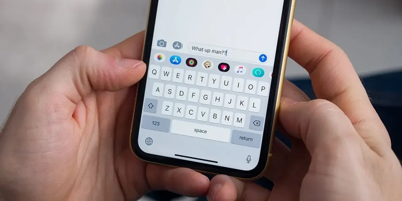 Mani che tengono uno smartphone. La tastiera mostra come togliere la maiuscola per scrivere "What up man??".