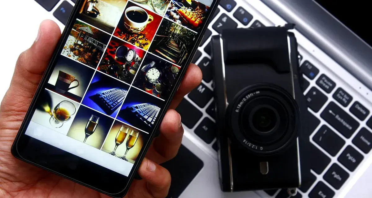 Smartphone con galleria foto su tastiera laptop, accanto a fotocamera. Guida rapida per scaricare le foto dal cellulare al pc.