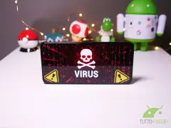 Schermo di un telefono con avviso "VIRUS" e teschio. Sullo sfondo, pupazzi di Android e Pokémon, con lucine.