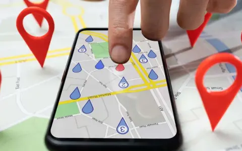 Dita la mappa con puntatori rossi, un dito tocca uno smartphone che mostra una mappa con gocce d'acqua, simulando gli spostamenti su Google Maps.