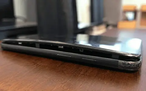 Il telefono è danneggiato, con lo schermo che si stacca dal corpo. Si vede la cornice interna e i pulsanti laterali.