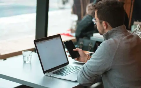 Uomo con occhiali che usa il telefono e il laptop, scopri come collegare il telefono al pc senza cavo per una maggiore comodità.