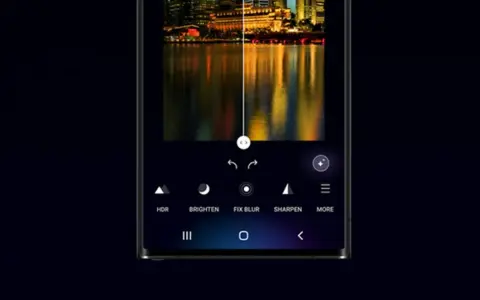 Interfaccia di editing foto su smartphone, con un paesaggio urbano notturno diviso a metà. L'opzione "galaxy enhance-x" migliora la nitidezza e i colori.