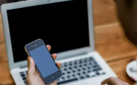Persona che cerca su un laptop come attivare il microfono su Google, tenendo in mano uno smartphone.