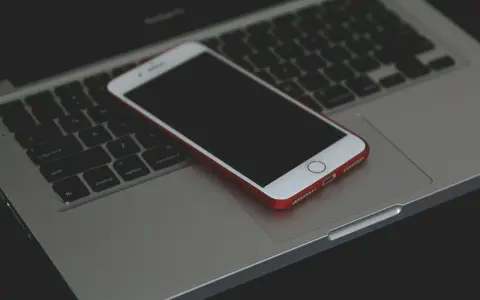 Un iPhone con cover rossa giace spento sulla tastiera di un MacBook.