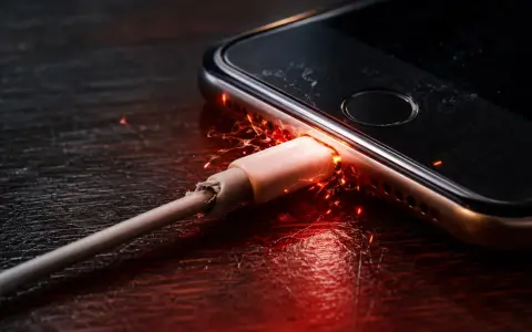 Un cavo di ricarica danneggiato provoca scintille e fiamme vicino alla porta del telefono, suggerendo una scheda madre del telefono bruciata.