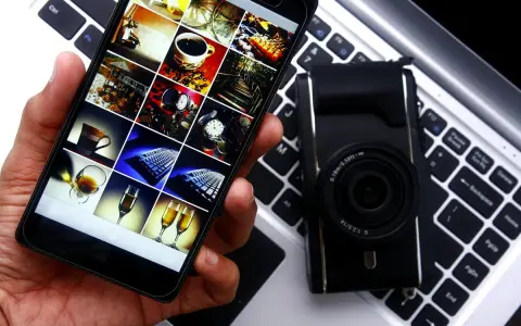 Smartphone con galleria foto su tastiera laptop, accanto a fotocamera. Guida rapida per scaricare le foto dal cellulare al pc.