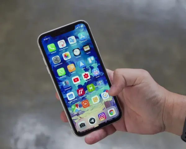 Mano che tiene uno smartphone con icone app. Potrebbe indicare problemi dopo sostituzione display, con alcune icone che appaiono leggermente sfocate o distorte.