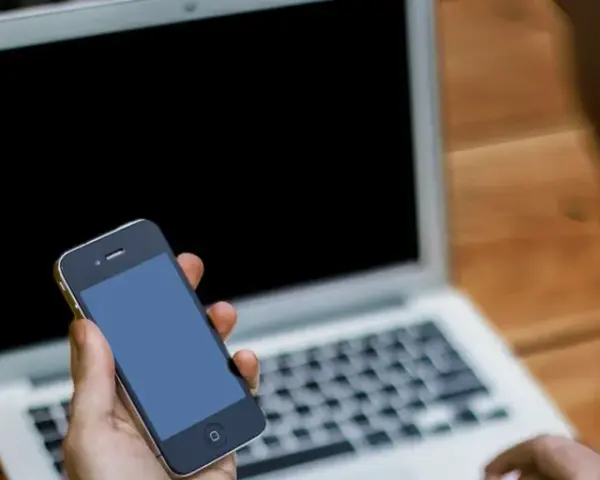 Persona che cerca su un laptop come attivare il microfono su Google, tenendo in mano uno smartphone.