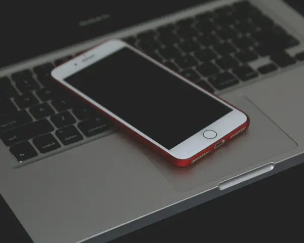 Un iPhone con cover rossa giace spento sulla tastiera di un MacBook.