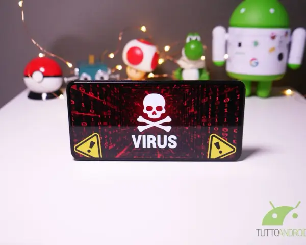 Schermo di un telefono con avviso "VIRUS" e teschio. Sullo sfondo, pupazzi di Android e Pokémon, con lucine.