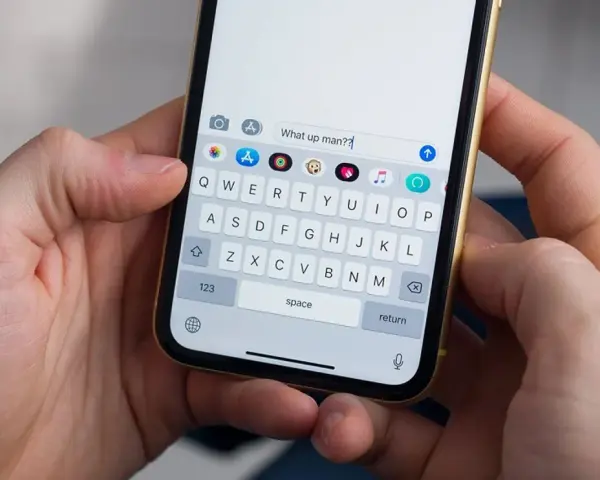 Mani che tengono uno smartphone. La tastiera mostra come togliere la maiuscola per scrivere "What up man??".