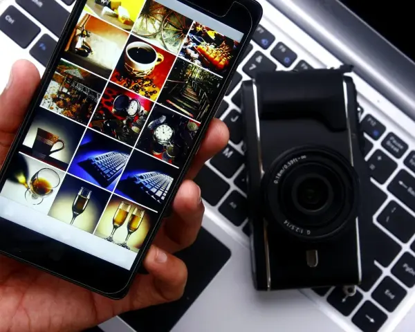 Smartphone con galleria foto su tastiera laptop, accanto a fotocamera. Guida rapida per scaricare le foto dal cellulare al pc.