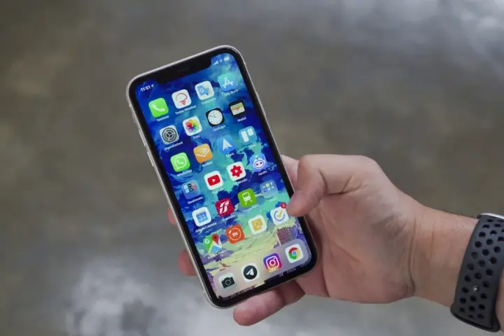 Mano che tiene uno smartphone con icone app. Potrebbe indicare problemi dopo sostituzione display, con alcune icone che appaiono leggermente sfocate o distorte.