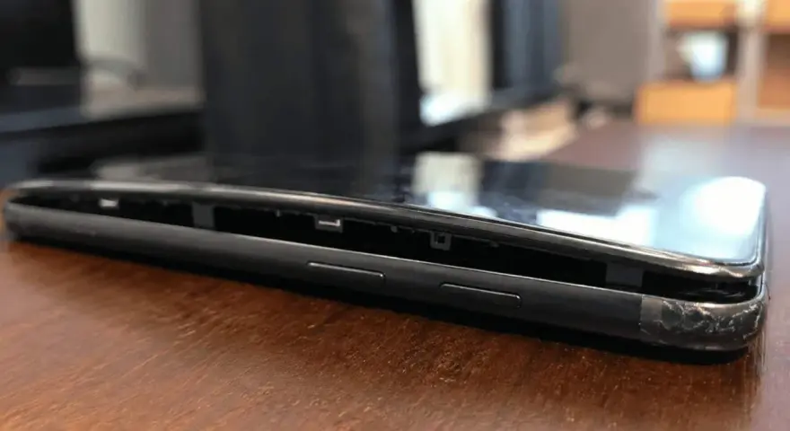 Il telefono è danneggiato, con lo schermo che si stacca dal corpo. Si vede la cornice interna e i pulsanti laterali.