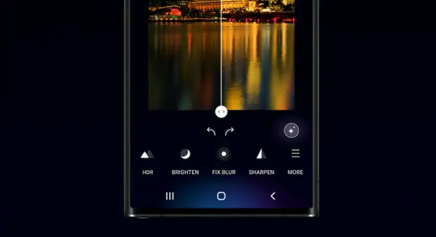 Interfaccia di editing foto su smartphone, con un paesaggio urbano notturno diviso a metà. L'opzione "galaxy enhance-x" migliora la nitidezza e i colori.