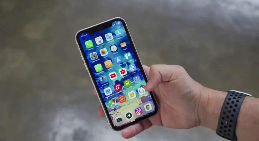 Mano che tiene uno smartphone con icone app. Potrebbe indicare problemi dopo sostituzione display, con alcune icone che appaiono leggermente sfocate o distorte.
