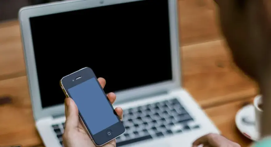 Persona che cerca su un laptop come attivare il microfono su Google, tenendo in mano uno smartphone.