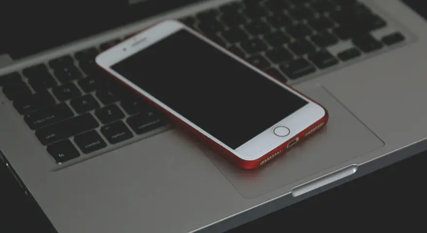 Un iPhone con cover rossa giace spento sulla tastiera di un MacBook.