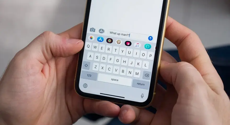 Mani che tengono uno smartphone. La tastiera mostra come togliere la maiuscola per scrivere "What up man??".