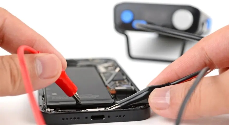 Mani che collegano cavi a un iPhone aperto, un esempio di riparazione fai-da-te con iFixit Italia.