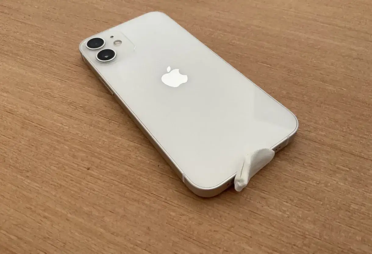 iPhone bianco su tavolo di legno, con un pezzo di nastro bianco che copre la porta di ricarica. Problema: iphone non si sente audio chiamata solo vivavoce.