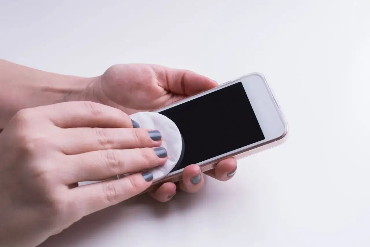 Mani che puliscono lo schermo di uno smartphone con un dischetto di cotone. Speriamo che il touch telefono non funzioni più a causa dello sporco.
