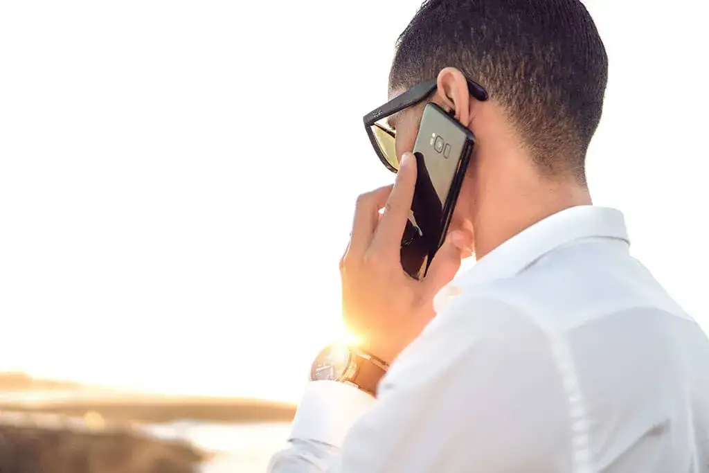 Uomo con occhiali da sole parla al telefono, cercando di capire come parlare con un operatore Wind non virtuale.