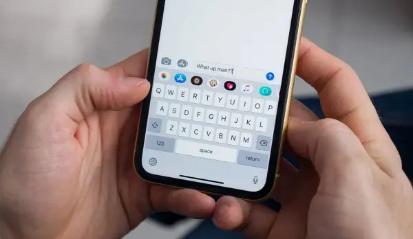 Mani che tengono uno smartphone. La tastiera mostra come togliere la maiuscola per scrivere "What up man??".